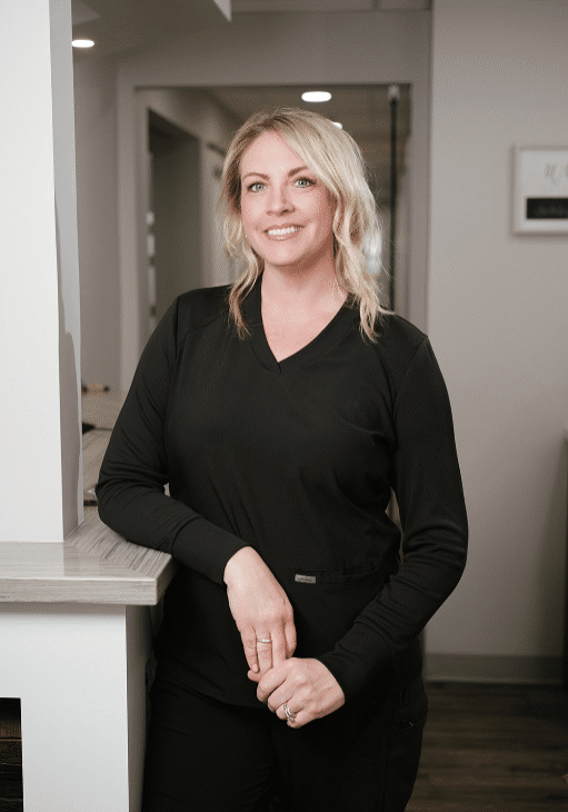 Smiling woman in black scrubs leaning on a clinic reception counter in a bright hallway.