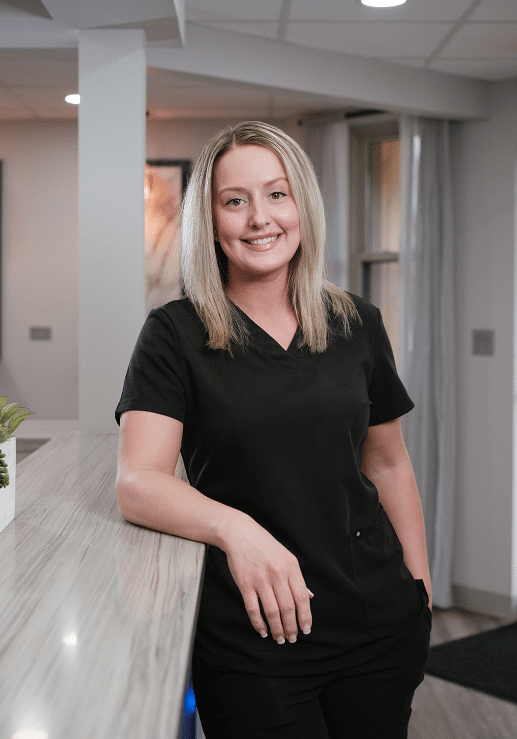 Smiling healthcare professional in black scrubs leaning on a light marble reception counter in a modern clinic.